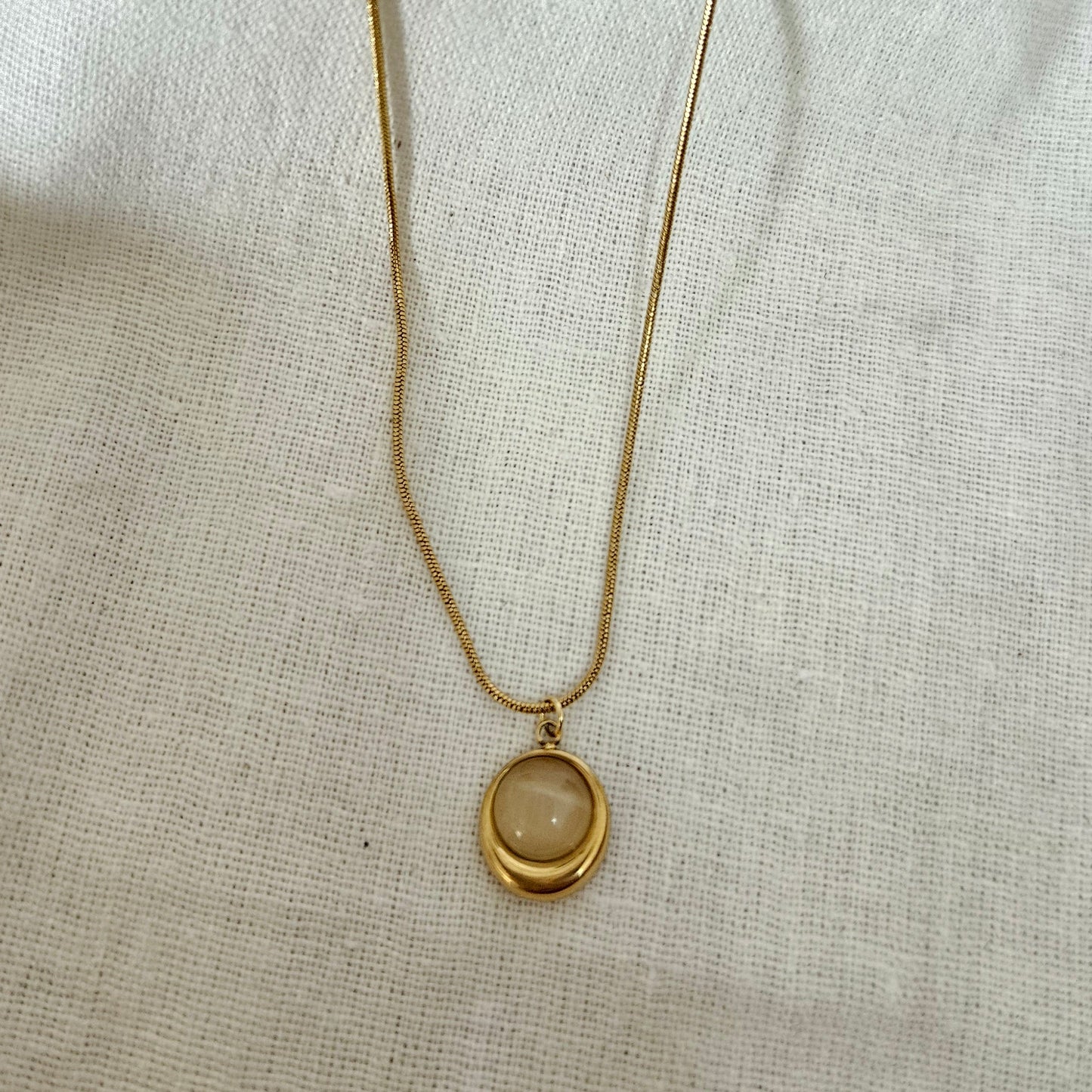 Gold necklace with a round pendant on a light fabric background